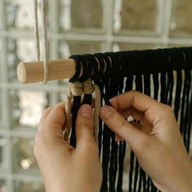 manos creando un adorno tejido de macramé negro y gris