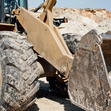 Close-up of a massive wheel loader tire and bucket joint in a quarry, warm metallic tones