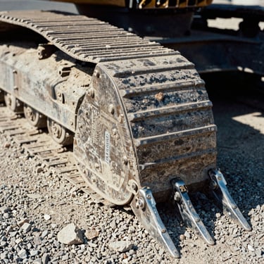 Macro shot of heavy excavator bucket teeth resting on gravel, high-contrast sunlight