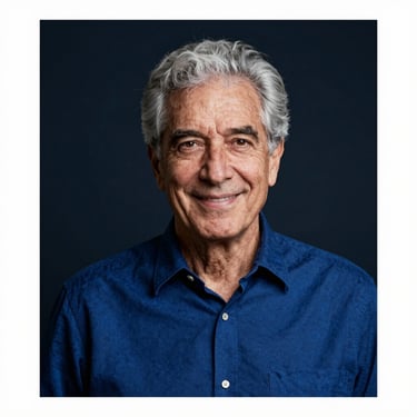 A professional portrait of a senior man with grey hair in a deep royal blue shirt. He has a warm, trustworthy smile, set against a dark navy background.