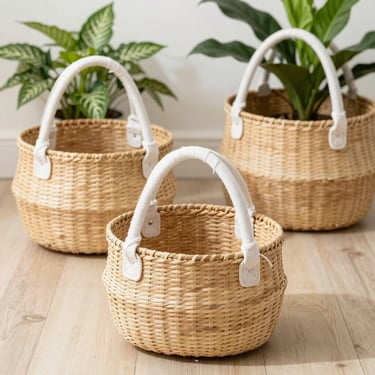 Set of three nesting seagrass baskets with white cotton handles on a light wooden floor, bright daylight