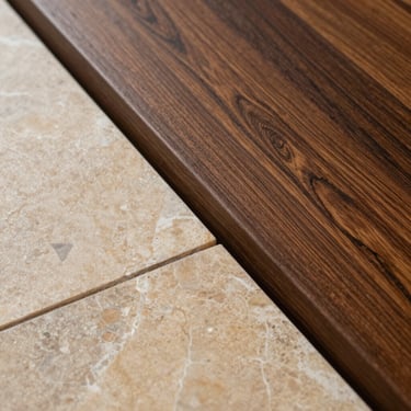 Overhead macro of a stone-to-wood threshold transition — warm limestone tile meeting dark oiled oak, precise cut line, natural daylight from the left, no props