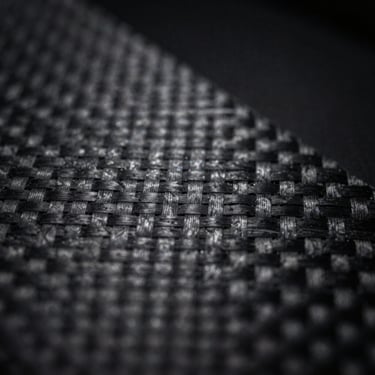 Macro shot of technical carbon weave fabric, low-key lighting, sharp directional light highlighting texture