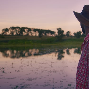 Farmer standing by a river at sunset in The Farm We Call Home film.