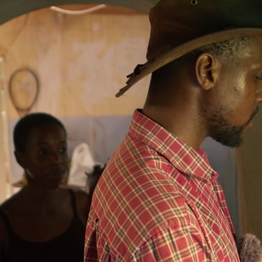 Interior scene of a farmer in an archway with another figure behind in The Farm We Call Home film.