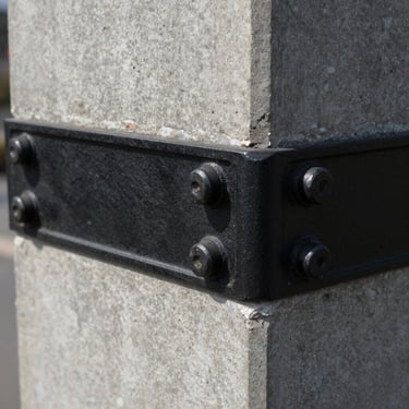 Close-up of a blackened steel joint bolted into a concrete pillar
