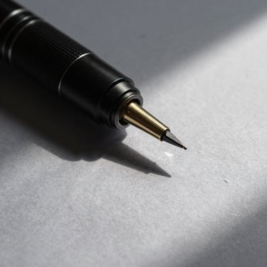 Plano detalhe de uma caneta tinteiro clássica sobre papel texturizado cinza, iluminação natural lateral fria com sombras geométricas nítidas.
