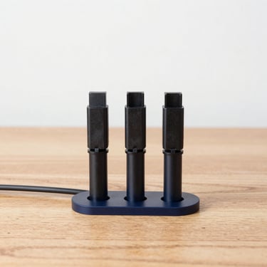 A sleek minimalist magnetic cable organizer holding three black cables on a wooden desk, crisp details
