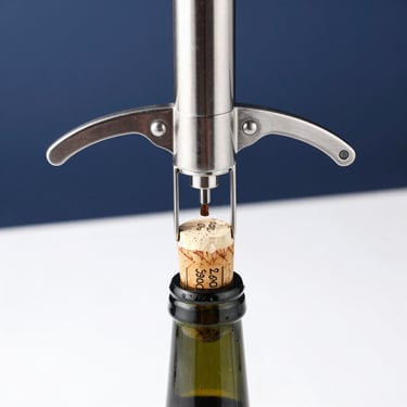 Close-up of an elegant stainless steel electric wine opener extracting a cork from a bottle, bright studio lighting with soft shadows, minimalist dark blue background accent