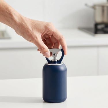 Close-up of a hand demonstrating a modern automatic jar opener on a clean kitchen counter, bright studio lighting