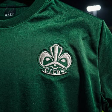 Close-up of premium embroidered club crest on dark green fabric, sharp shadows.