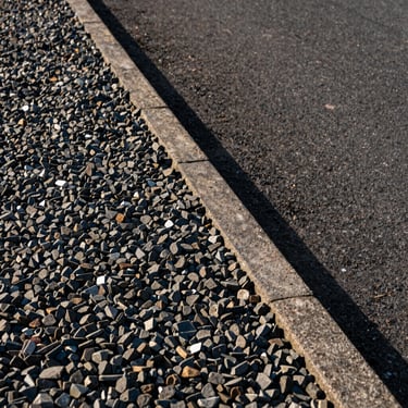 Detail shot of freshly laid gravel path edge meeting a stone border, late afternoon natural light, no people, sharp material texture, tight documentary crop