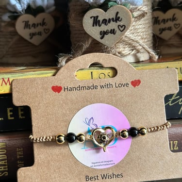 Pulsera tejida con perlas negras y un corazon con libros y velas de fondo