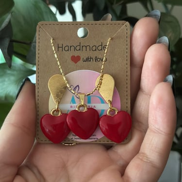 Set de aretes y collar de corazon rojo con fondo unas plantas