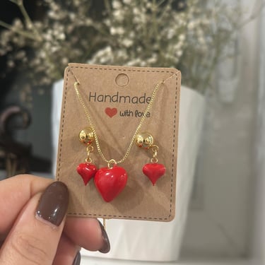 Set de collar y corazon pequenos de color rojo con fondo de flores