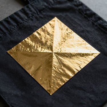 Macro shot of metallic gold heat transfer vinyl pressed onto a dark canvas tote bag, showing sharp geometric corners.