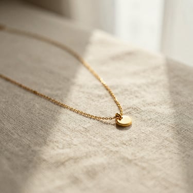Macro shot of a delicate gold necklace resting on a textured linen surface, warm morning light