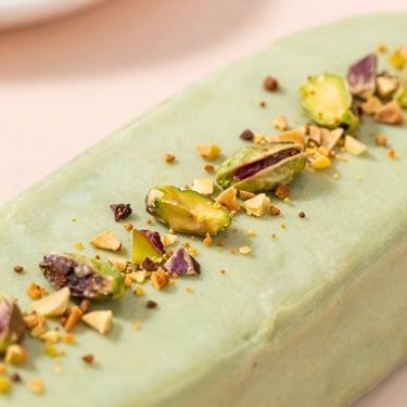 Close-up of a creamy pistachio green paleta sprinkled with crushed roasted pistachios, soft daylight, pastel background