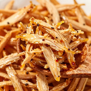 Close-up of shredded chicken pickle glistening with oil and spices on a wooden spoon, high-contrast texture.