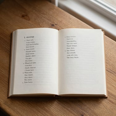 Overhead flat-lay of a single open poetry book on a warm wooden surface, shallow depth of field