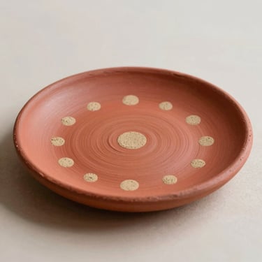 Macro shot of a hand-painted red clay plate with sand-colored dots, soft side-light, minimalist neutral background