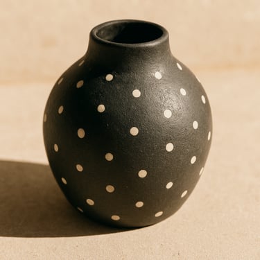 Minimalist dark ceramic vase with white dot patterns, styled flat-lay in a sun-drenched neutral interior, soft shadows