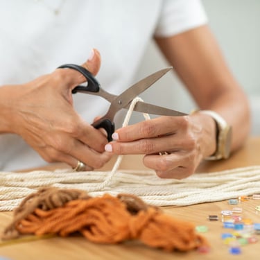Manos de mujer con tijeras cortando cuerda de macramé