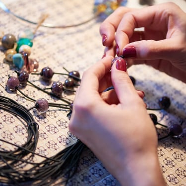 Manos de mujer tejiendo pulseras con piedras naturales