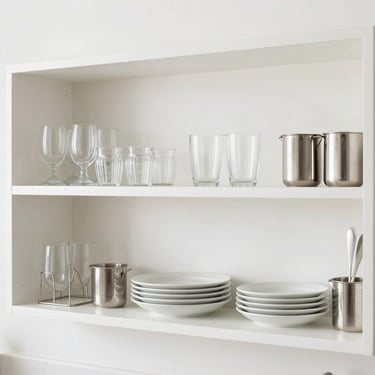 Clean modern kitchen shelves with organized glassware, ceramic plates, and stainless steel tools, bright daylight, 35mm
