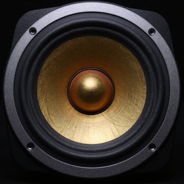 Macro shot of a high-end speaker driver, golden copper coil visible, brushed aluminum housing, dramatic low-key lighting.