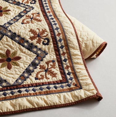 An artistic shot of the quilt partially folded on a clean, light surface, showing the contrast between the intricate front pattern and the solid warm cream backing.