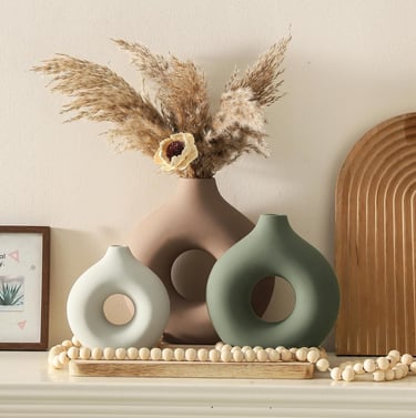 Three modern ceramic donut vases in neutral tones with dried pampas grass on a mantel.