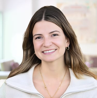 A smiling young woman with brown hair and gold jewelry wearing a white collared sweater.