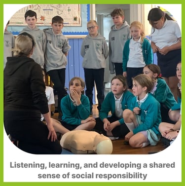 a group of children some sat down, some stood up around an instrictor with first aid equipment learn