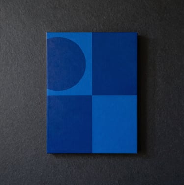 A portrait-oriented photograph of a finished artwork hanging in a high-end International / Urban Art Scene loft, featuring bold monochromatic blue shapes against a deep charcoal slate background.