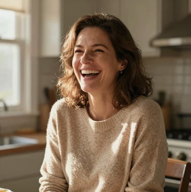 A warm, intimate portrait of a mother laughing in a sun-lit North American / US kitchen. The light is soft and inviting, highlighting the soft sand tones of her sweater. Authentic and friendly atmosphere.