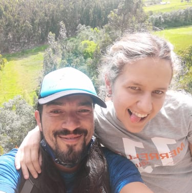 Smiling couple taking a selfie while hiking in a lush green valley with forest views.