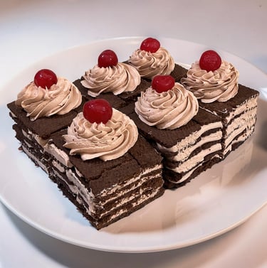 Miniature black forest cake slices with whipped chocolate cream and red cherries on a white plate.