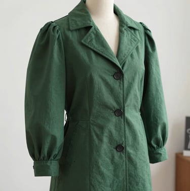 A garment mannequin draped in a structured forest green coat with whimsical puffed sleeves, Western / Global, set in a clean, brightly lit design studio.