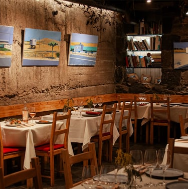 Rustic restaurant interior with white tablecloth settings, stone walls, and oil paintings.
