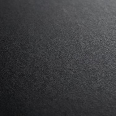 An abstract macro shot of high-quality paper texture with a subtle emboss, monochromatic black and dark grey tones, representing artisanal craftsmanship and premium quality.