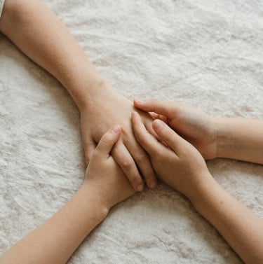 An artistic detail shot of a parent and child's hands intertwining, set against a soft off-white linen background. The lighting is warm and natural, creating a sense of intimacy and grace. North American style.