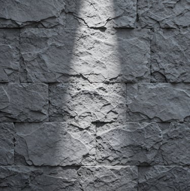 Texture study of a weathered grey stone wall with a single direct beam of light hitting the center, elegant, quiet, using #D0D5DB and #2F363F.