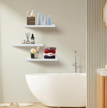 Modern white floating shelves installed above a white bathtub holding skincare products and folded towels.