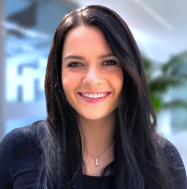 Smiling woman with long dark hair wearing a black shirt and necklace in a professional office setting.