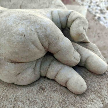 Close-up of a white marble sculpture depicting a chubby baby hand resting on a rock.