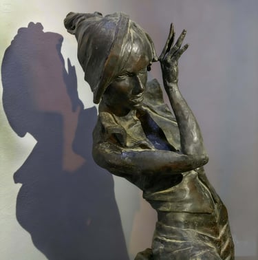 Bronze sculpture of a woman in a headscarf casting a dramatic shadow on a white wall.