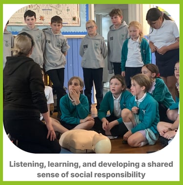 a group of children some sat down, some stood up around an instrictor with first aid equipment learn