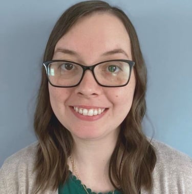 kristin gunner, doula, with glasses, smiling in front of a blue background