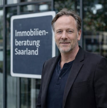 Professional real estate consultant standing by an Immobilienberatung Saarland sign.